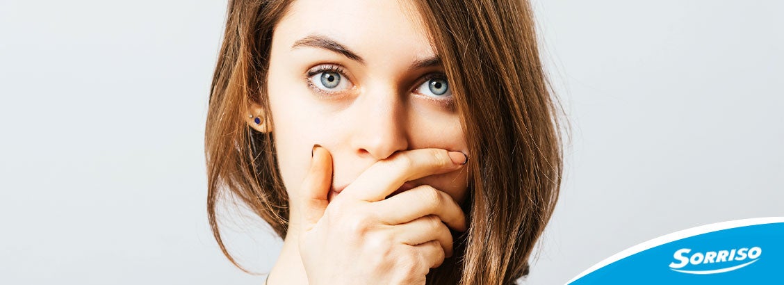 Mulher com a mão na boca devido às causas do mau hálito