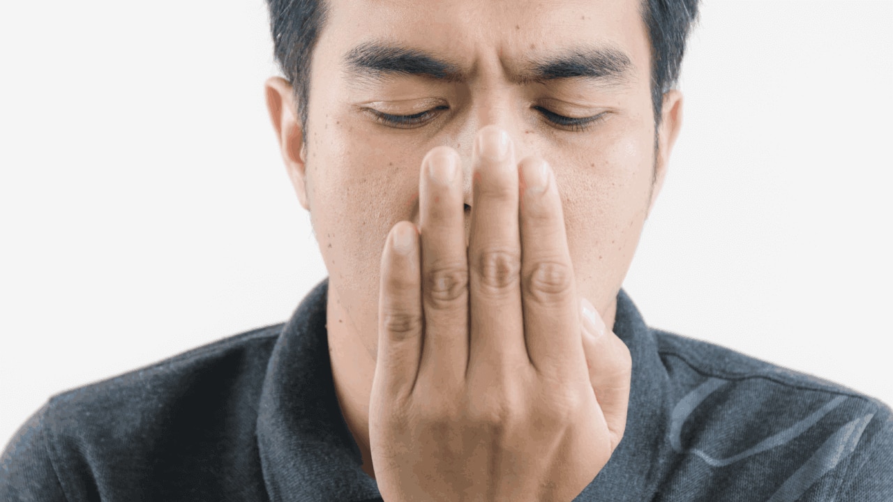 Homem com a mão em frente a boca, checando o hálito para descobrir se precisa de uma bala de hortelã